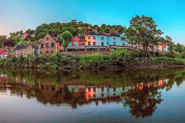 Une ville riveraine aux bâtiments aux couleurs vives, avec un pont et une végétation luxuriante.