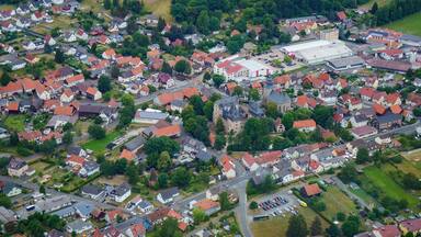 Vue aérienne d’un village européen avec des maisons aux toits rouges, une église et des champs environnants.