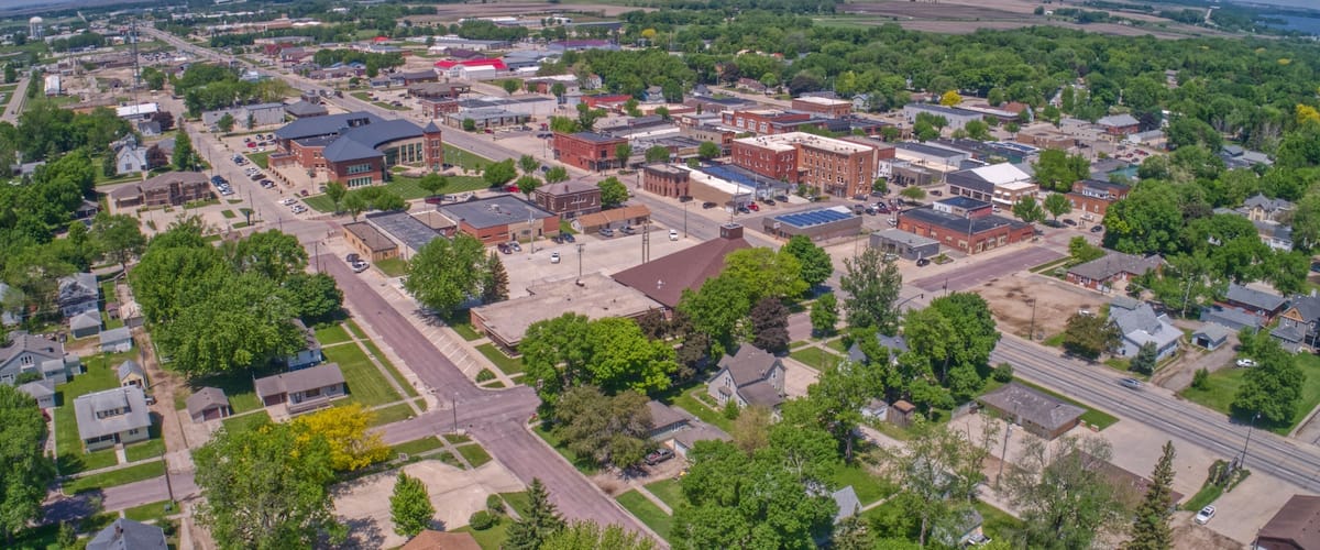 An aerial view of a town with a mix of residential and commercial buildings, roads, and green spaces.