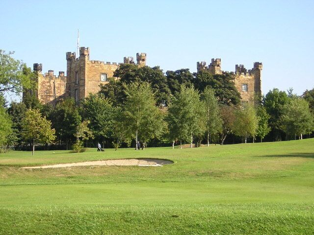 A castle with multiple towers and turrets, surrounded by a grassy field and trees.