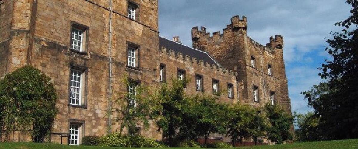 A historic castle with multiple towers and a well-maintained lawn.