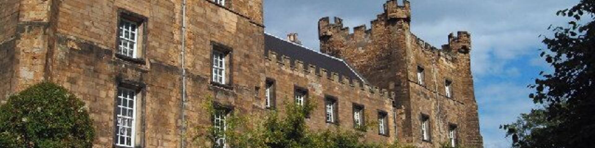 A historic castle with multiple towers and a well-maintained lawn.