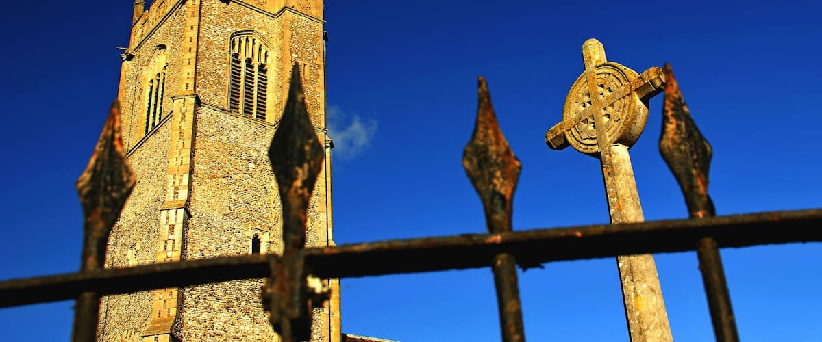 A historic stone tower with a pointed roof and a large arched window, set against a clear blue sky.