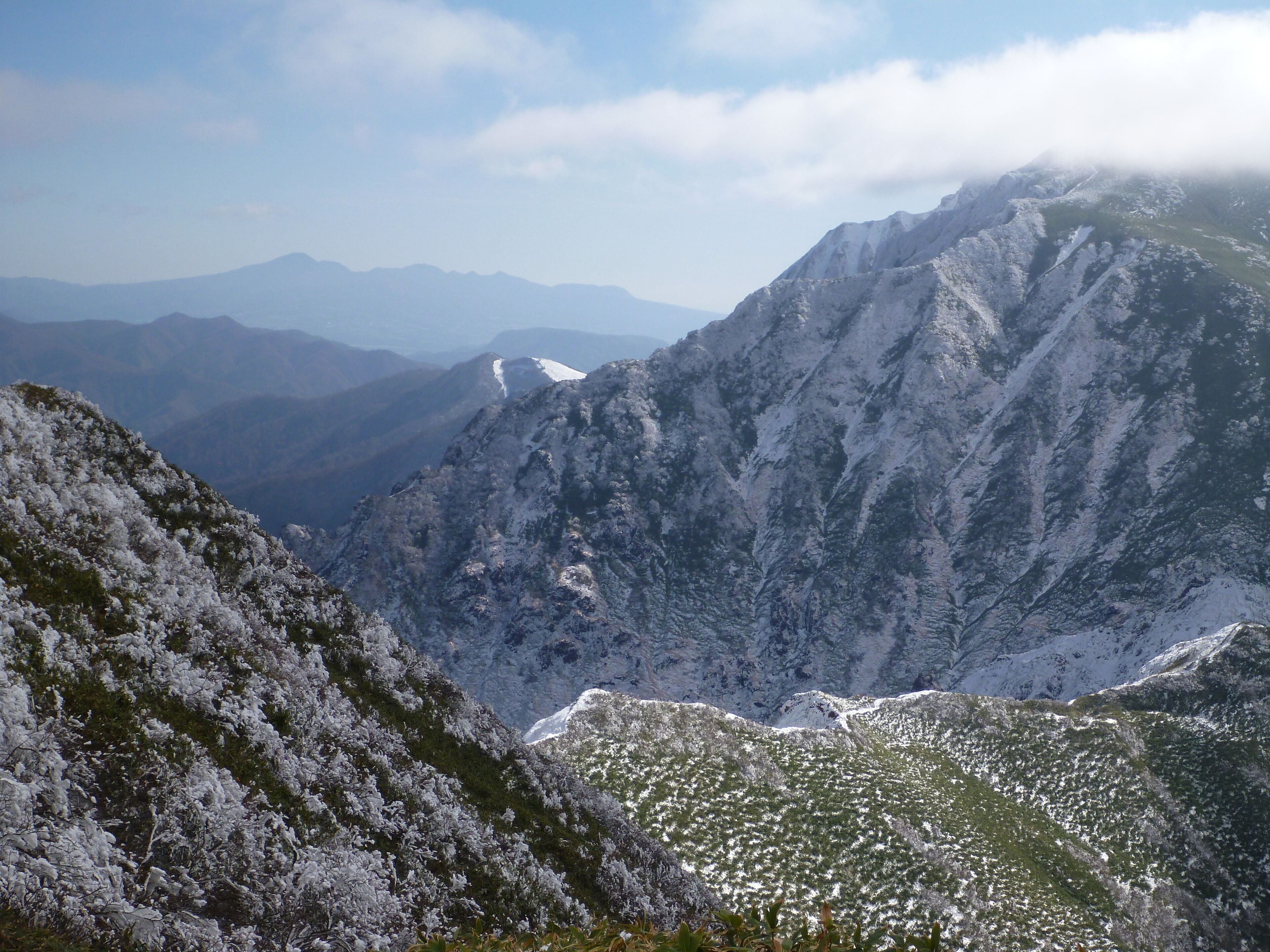 A snow-covered mountain range with a valley in the foreground and distant mountains under a clear sky.