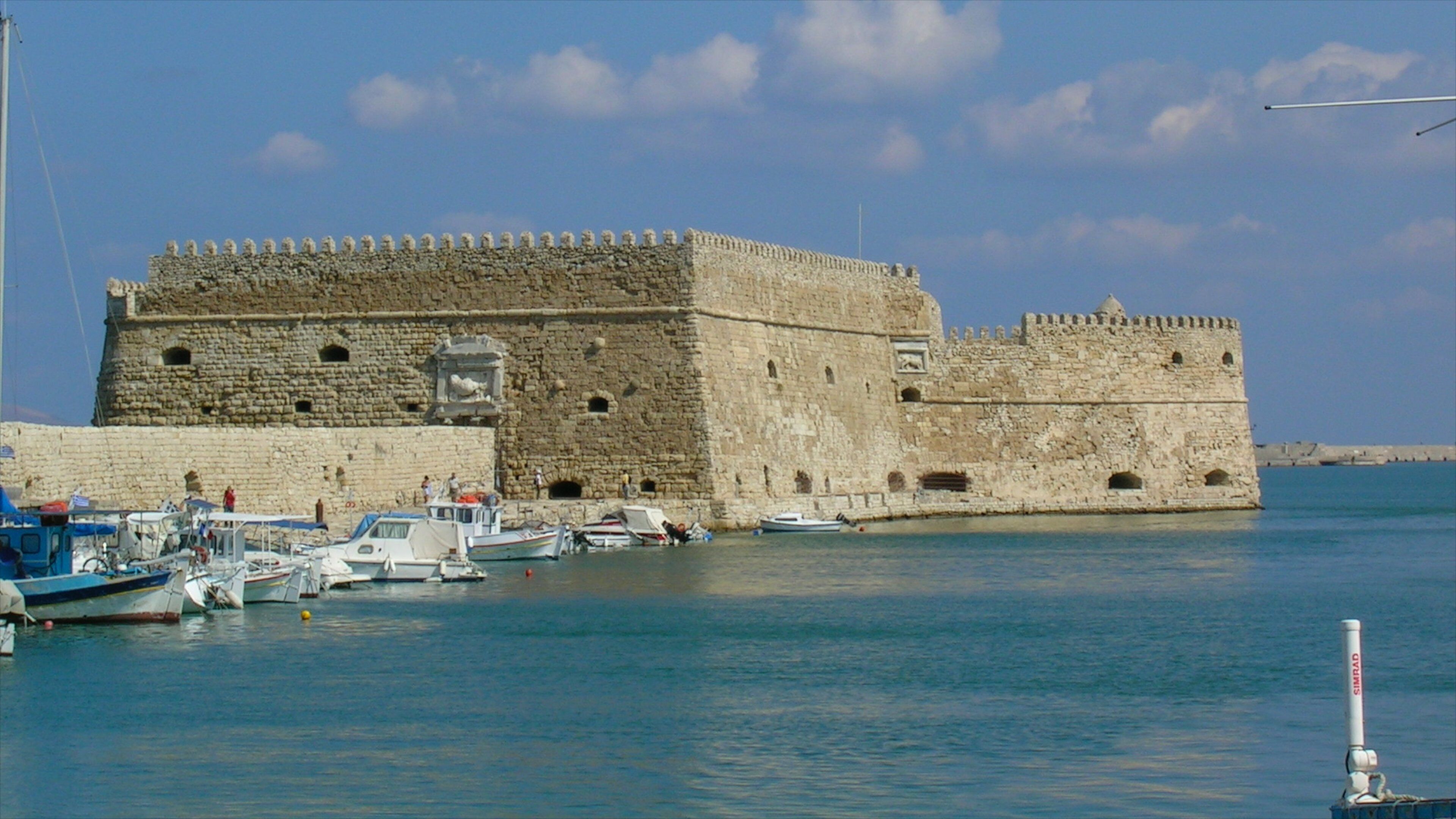 A historic stone fortress with a moat, surrounded by calm water and several boats.