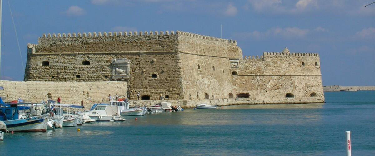 A historic stone fortress with a moat, surrounded by calm water and several boats.