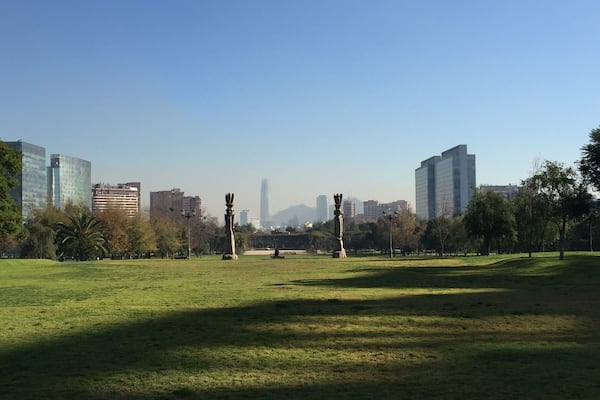Um parque com uma estátua, grama, árvores e edifícios modernos ao fundo.