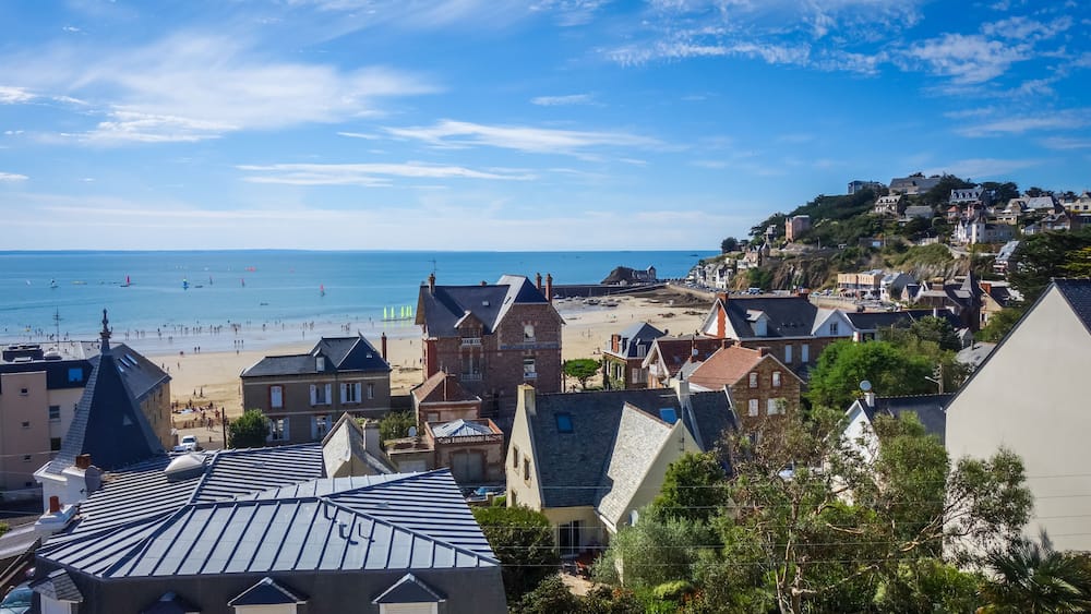 Une ville côtière avec une plage, des maisons et une colline sur laquelle se trouvent des bâtiments.