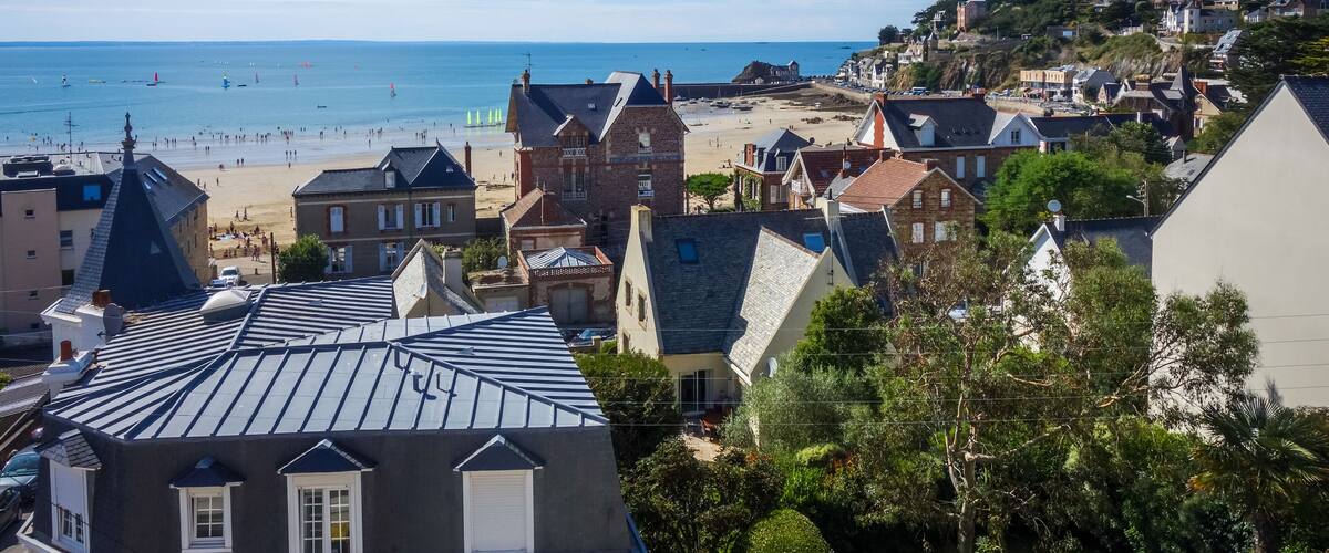 A coastal town with a beach, houses, and a hill with buildings.