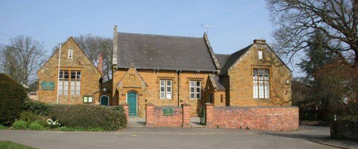 A traditional brick building with a slate roof, a green door, and a small garden area in front.