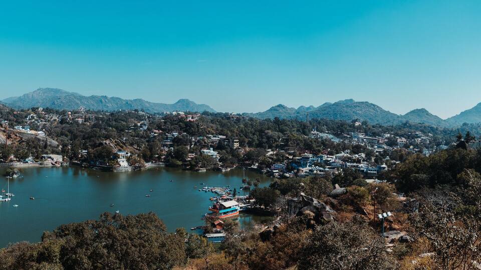 A lake surrounded by mountains, a town with buildings, and a lighthouse.