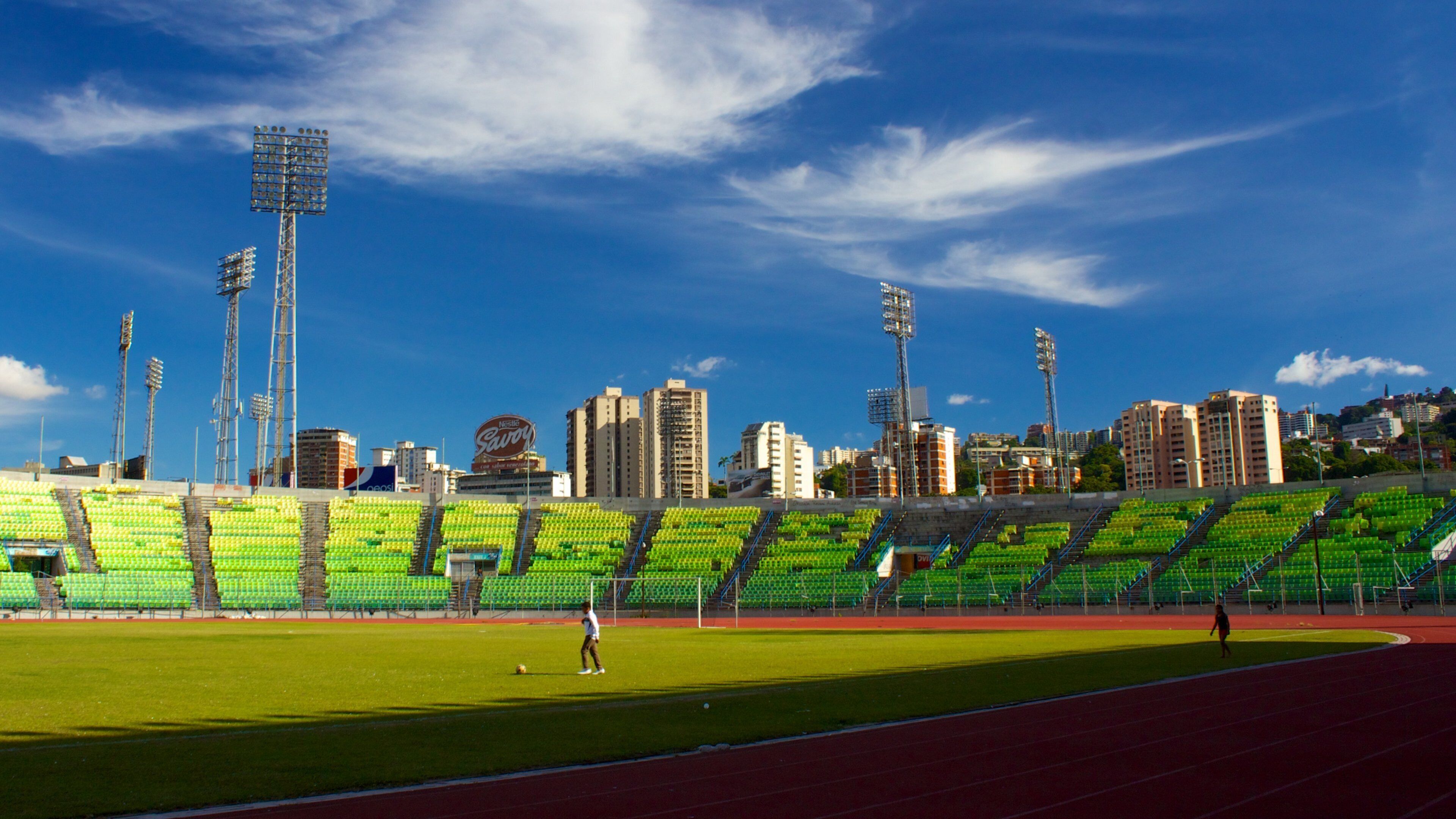 A stadium with green seats, a running track, and tall floodlights.