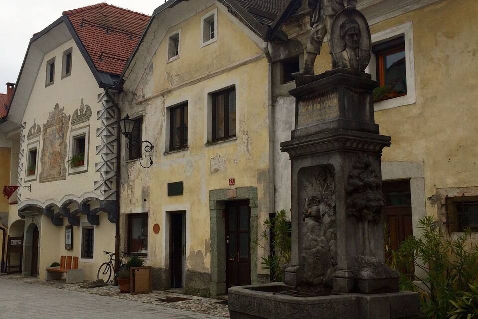 Una calle adoquinada con edificios históricos, una fuente y una estatua.