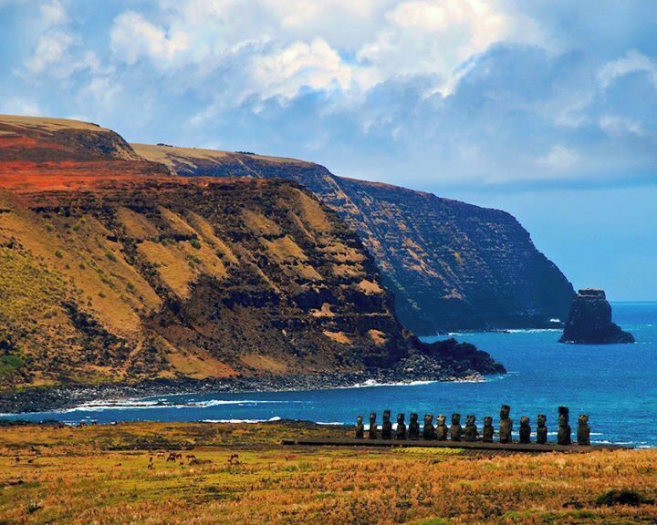 Paisagem costeira com um penhasco imponente, ondas do oceano e uma fileira de estátuas de pedra.