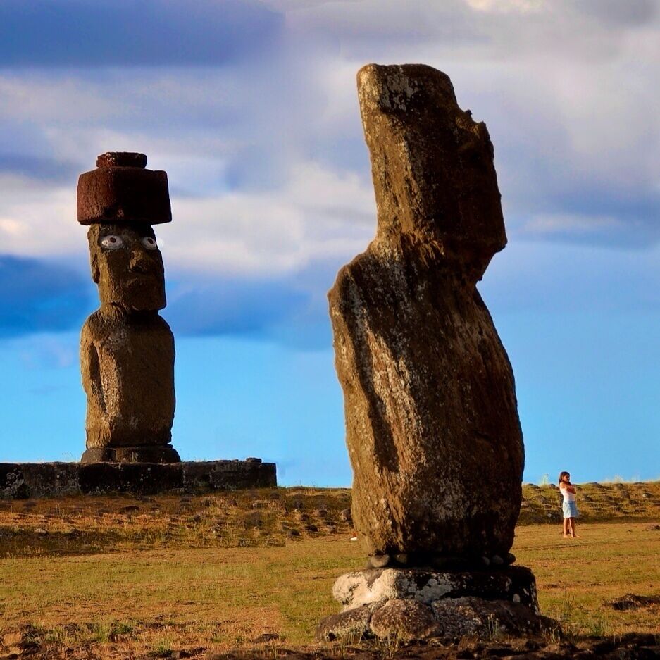Duas estátuas Moai na Ilha de Páscoa, com uma pessoa ao fundo.