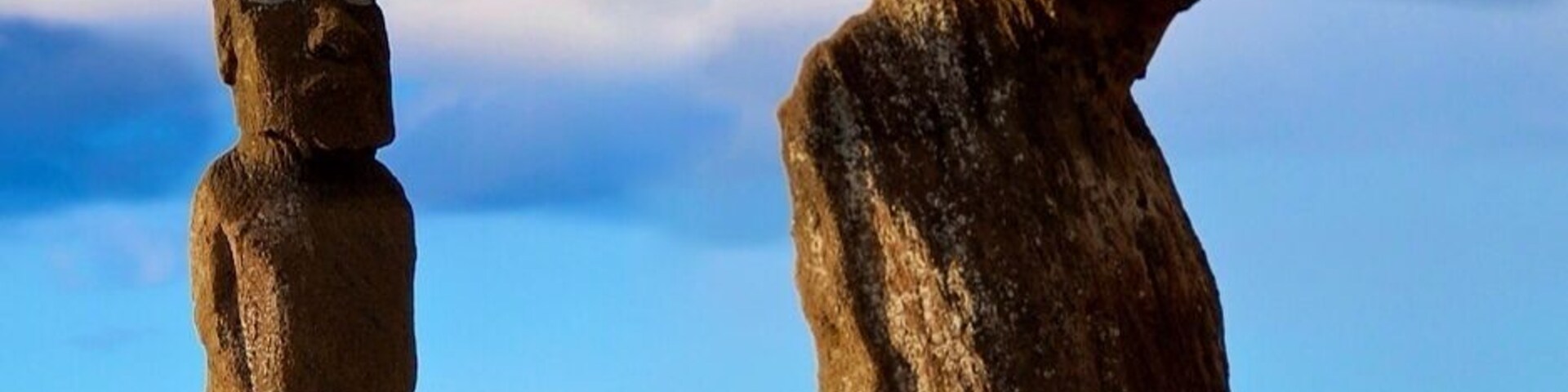 Duas estátuas Moai na Ilha de Páscoa, com uma pessoa ao fundo.
