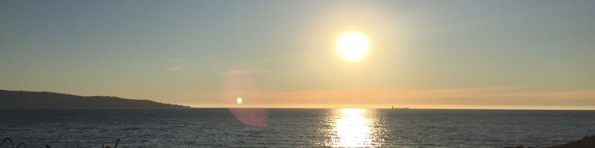 A sunset over a calm sea with a distant landmass.