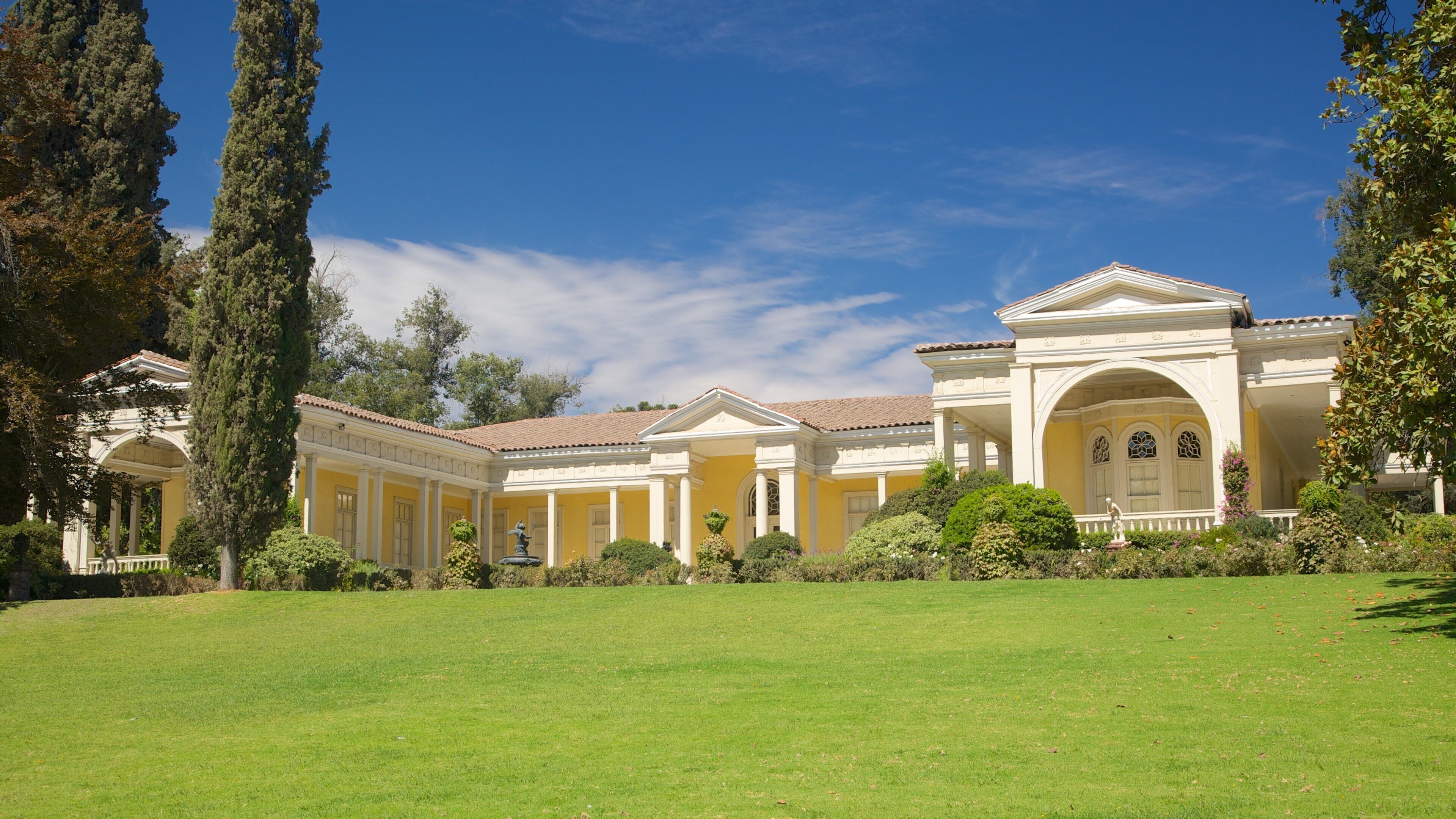 A large, yellow building with columns and a fountain in the center of a green lawn.