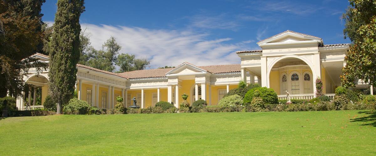 A large, yellow building with columns and a fountain in the center of a green lawn.