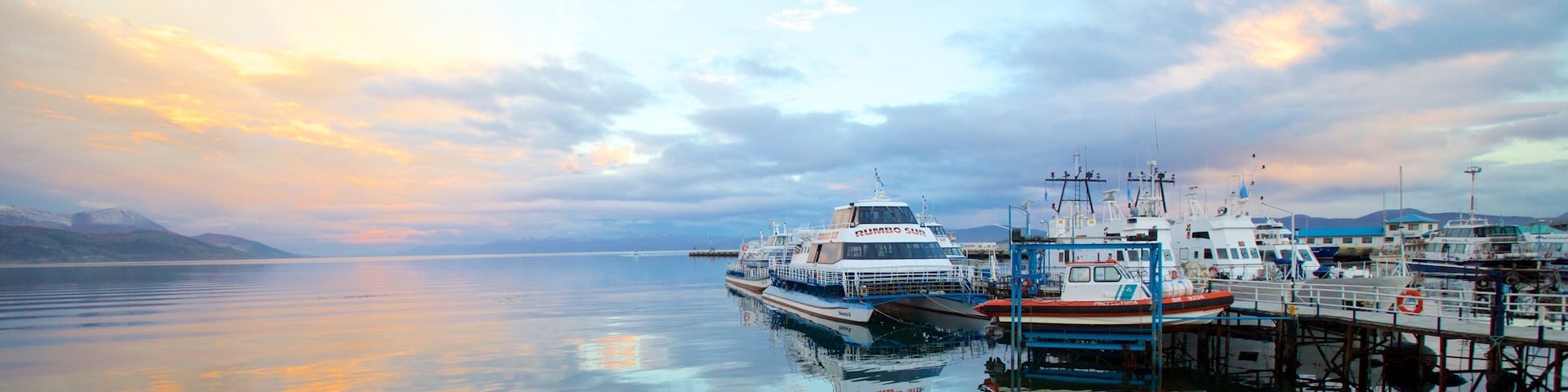 A marina with boats docked, calm water, and a sunset sky.