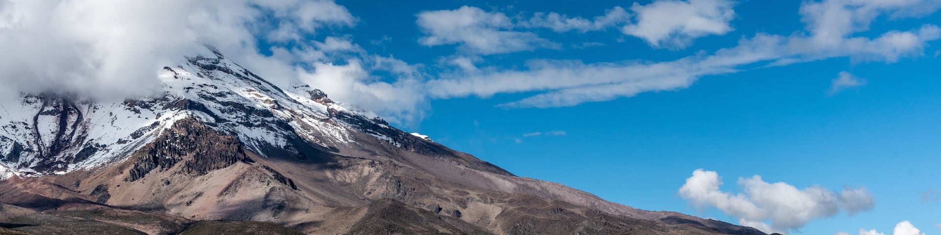 A snow-capped mountain, a clear blue sky, and a barren landscape.
