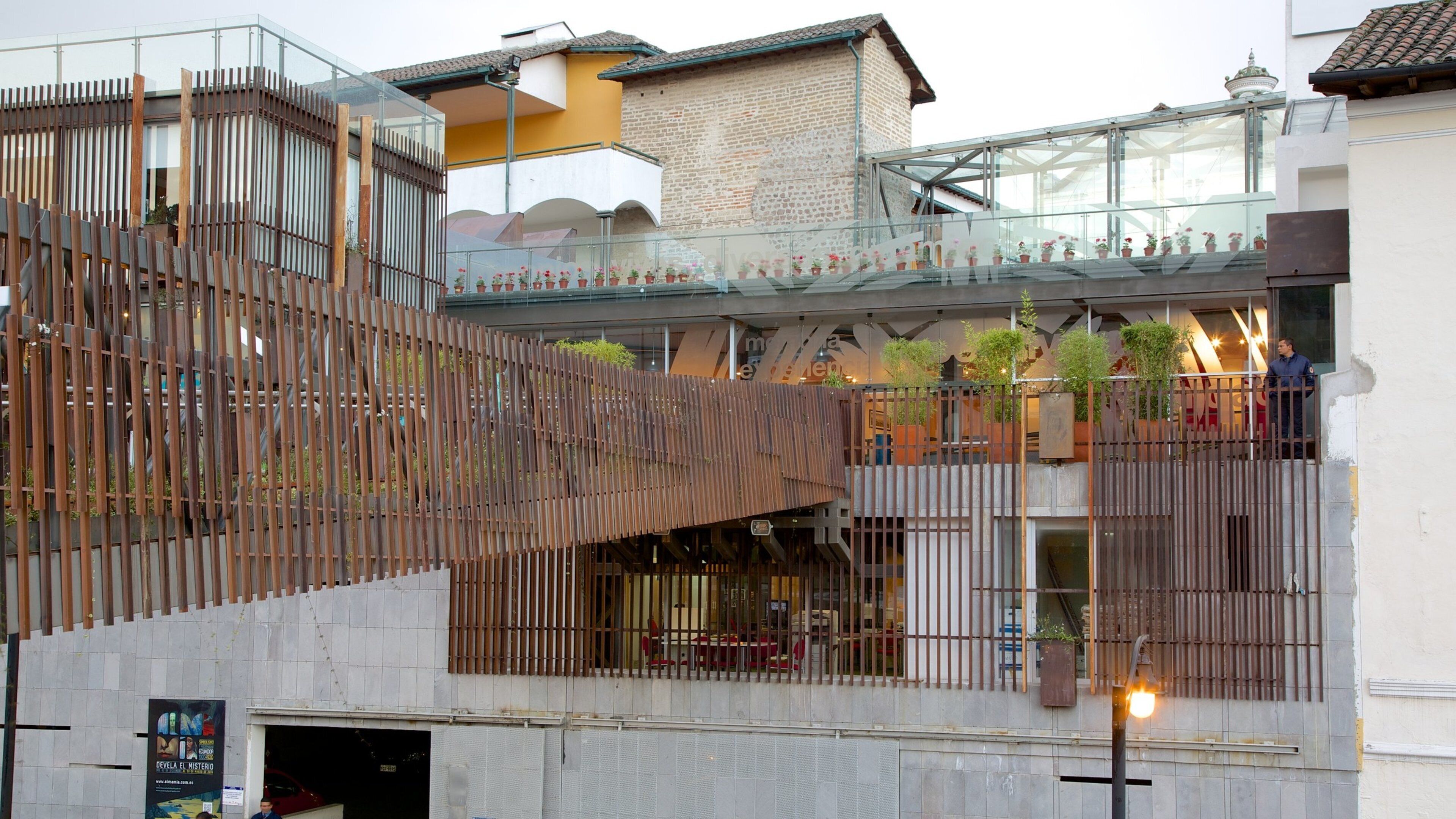 A modern building with a wooden slatted facade, a glass bridge, and potted plants.