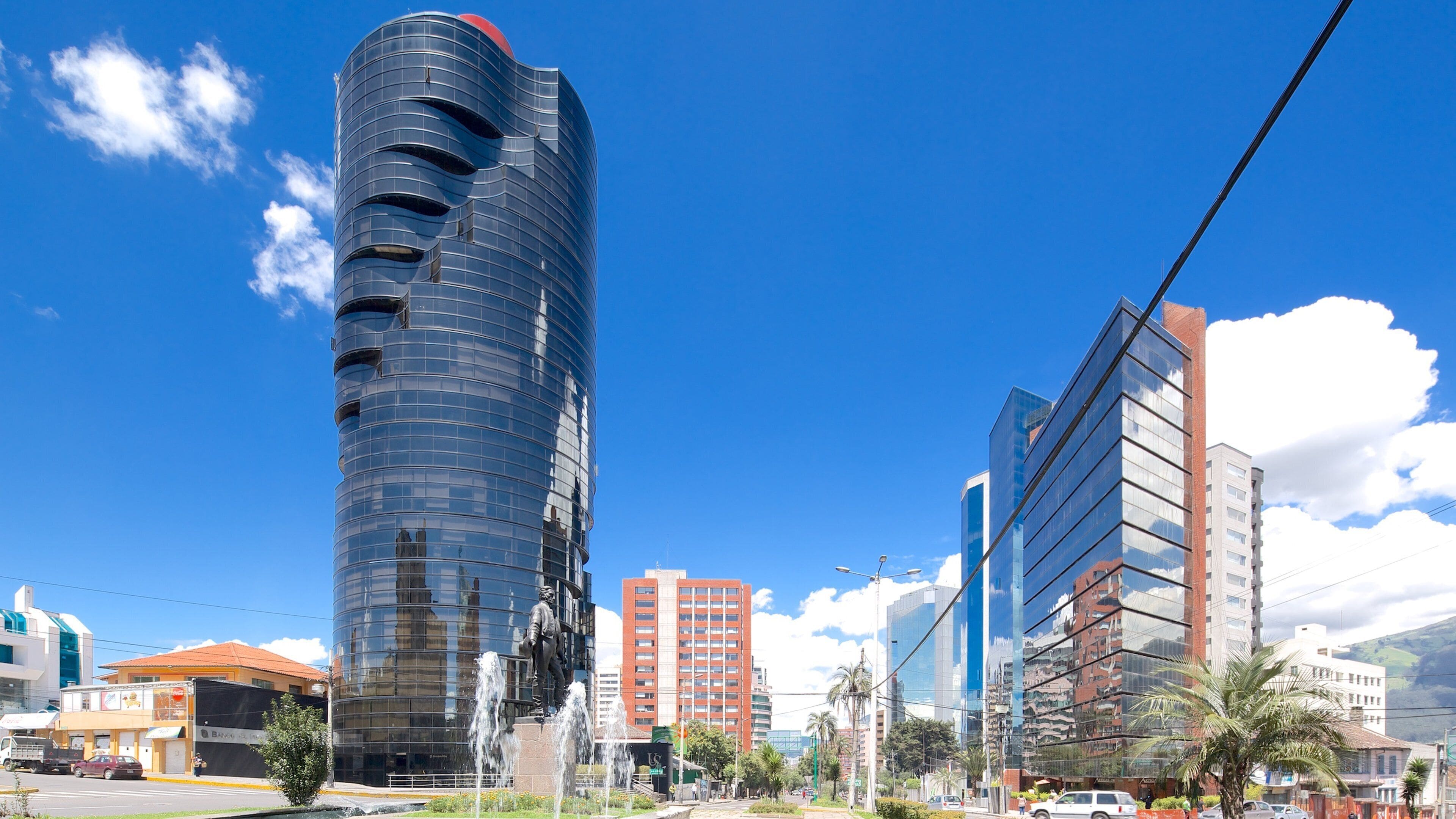 A modern cityscape with a distinctive curved skyscraper, a mix of modern and traditional buildings, and a clear blue sky.
