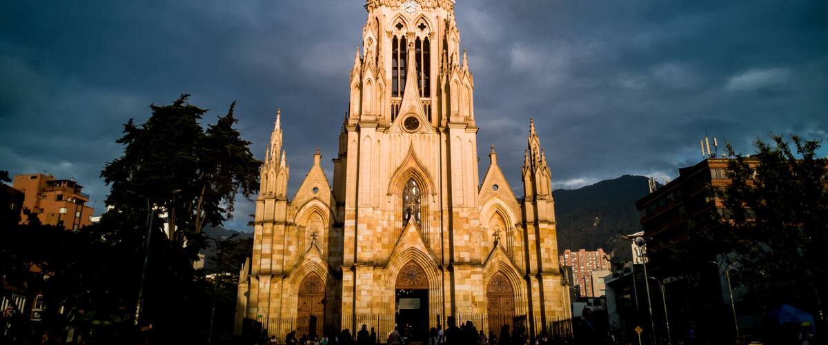 A Gothic-style cathedral with a clock tower, surrounded by trees and urban buildings.
