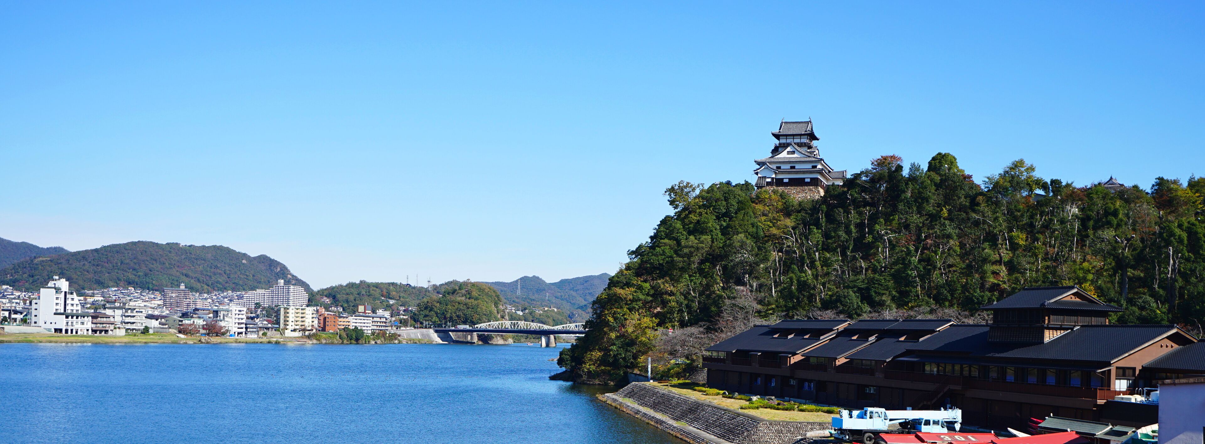 Una pagoda japonesa tradicional en una colina con vistas a un río, con edificios modernos y un puente al fondo.