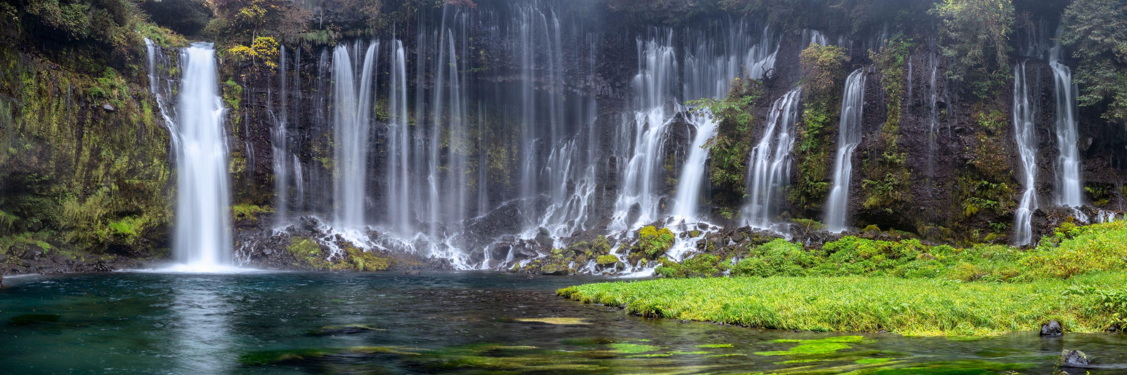 Una cascada en varios niveles que se precipita en una poza cristalina rodeada de exuberante vegetación.