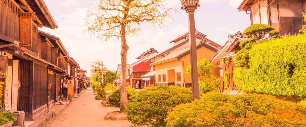 A traditional Japanese street with wooden buildings, a tree, and a street lamp.