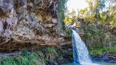 A waterfall cascading down a rocky cliff into a pool surrounded by lush greenery.