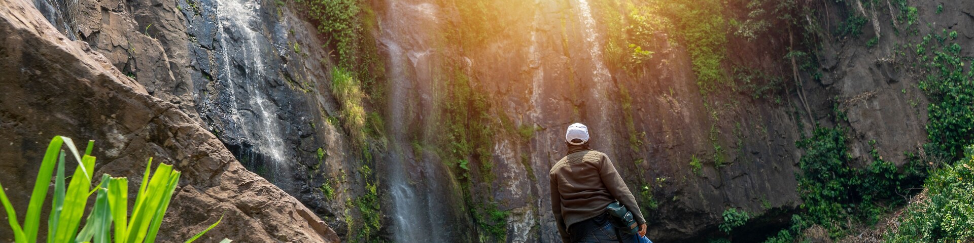 Una persona de pie sobre una roca, con una cascada al fondo.