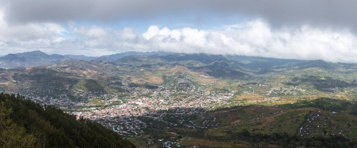 A mountainous landscape with a town nestled in the valley, surrounded by hills and under a cloudy sky.