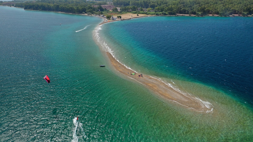 A coastal area with clear turquoise waters, a sandy beach, and a small lighthouse.