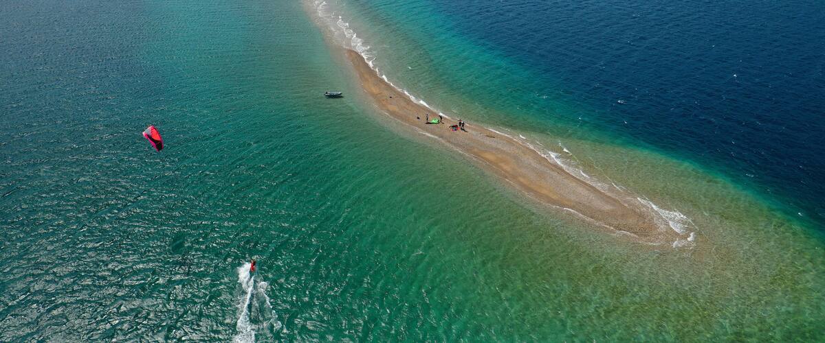 A coastal area with clear turquoise waters, a sandy beach, and a small lighthouse.