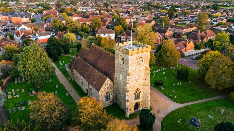 An aerial view of a town with a prominent church featuring a tall tower, surrounded by residential houses and a cemetery.