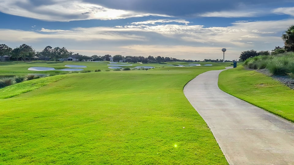 A golf course with a winding path, sand bunkers, and a distant flag.