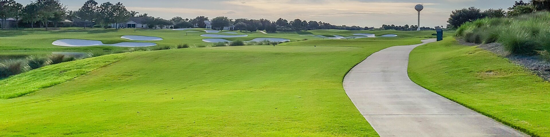 A golf course with a winding path, sand bunkers, and a distant flag.