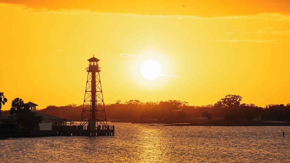 A lighthouse silhouetted against a sunset over a body of water.