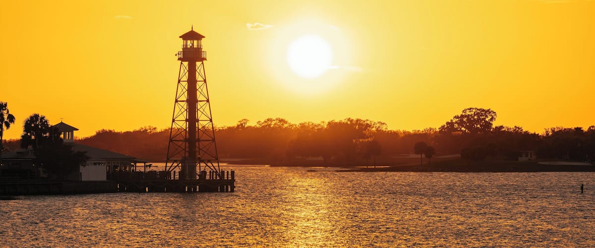 A lighthouse silhouetted against a sunset over a body of water.