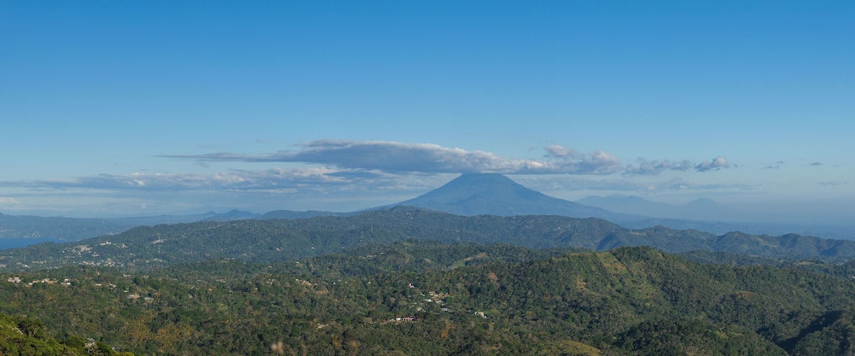 A mountain with a conical shape, surrounded by dense forest and a few scattered buildings.