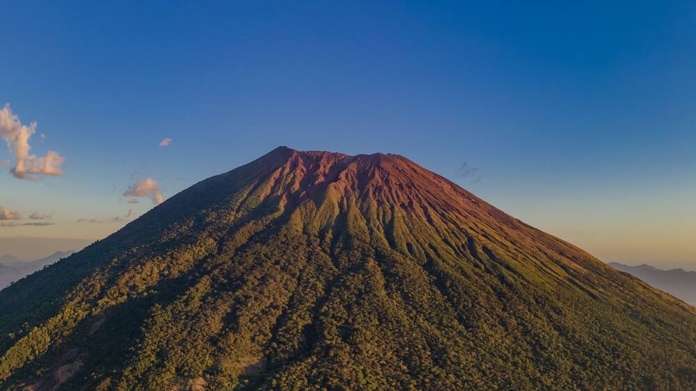 A volcano with a forested slope and a clear sky.