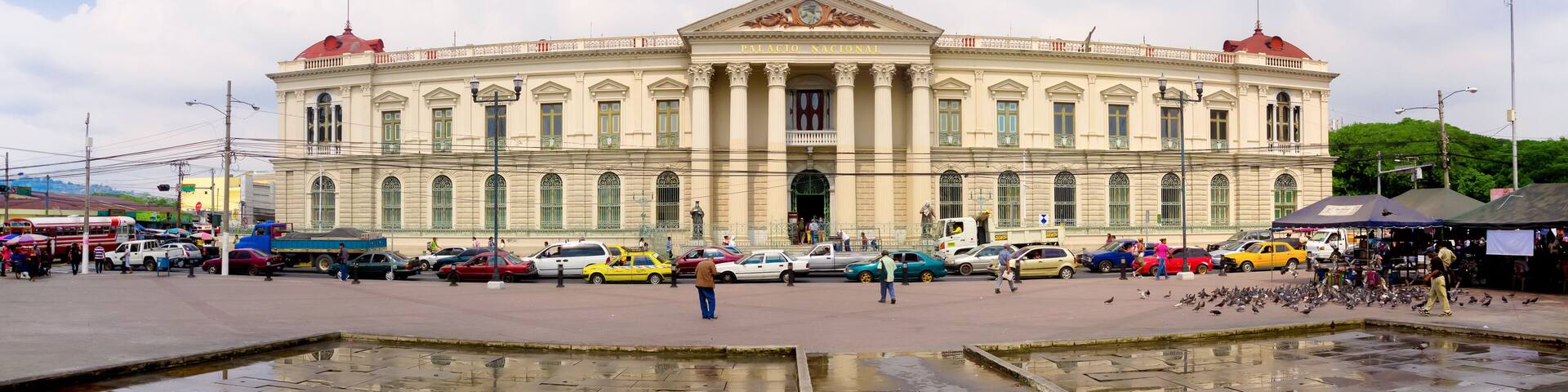 A large, historic building with a central dome and columns, surrounded by a busy street with cars and pedestrians.