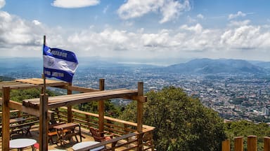 Une terrasse en bois avec des bancs, d’où l’on peut admirer une vue sur la ville et les montagnes. On aperçoit un drapeau du Salvador.