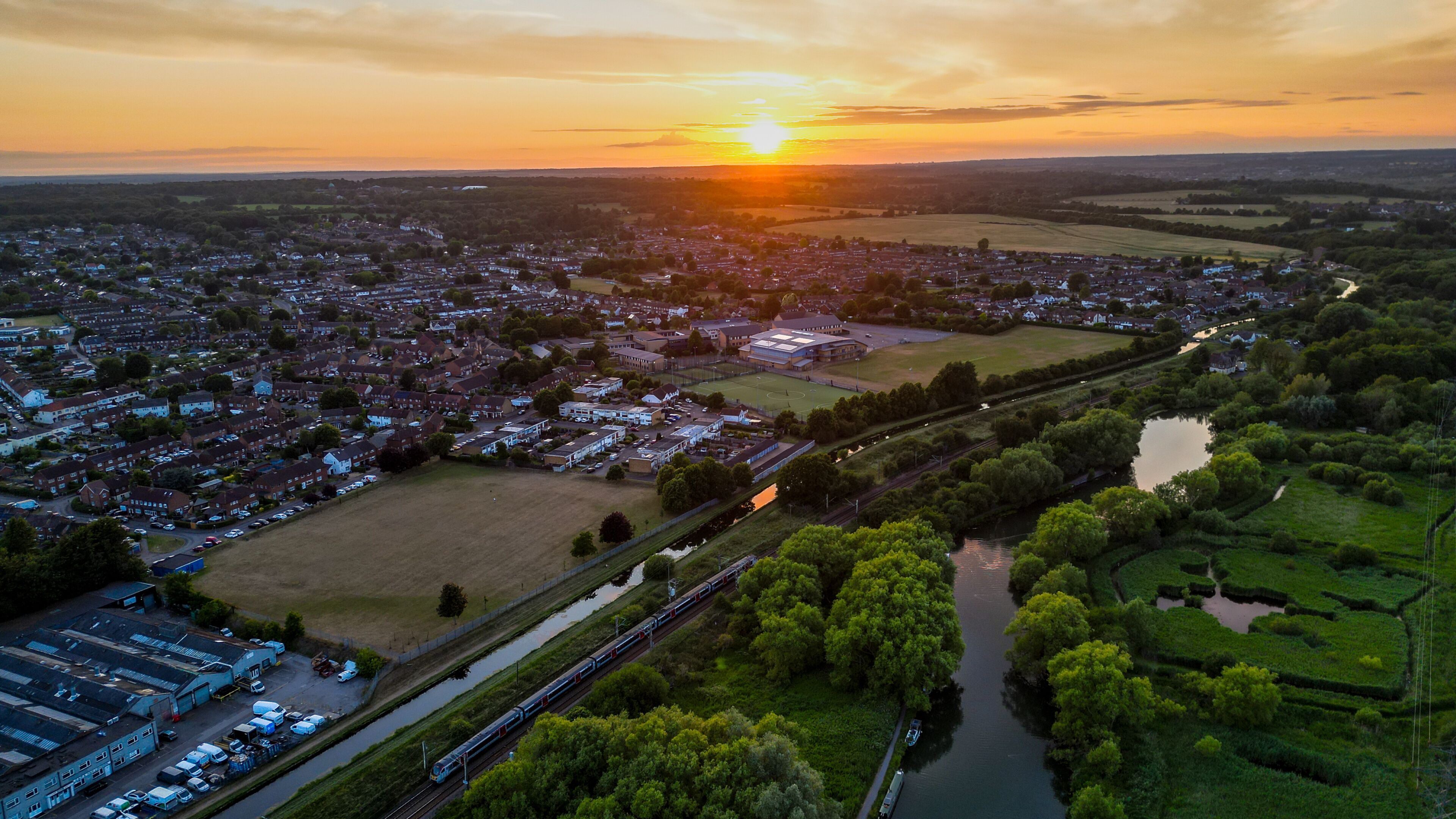 A sunset over a town with a river, train tracks, and surrounding greenery.