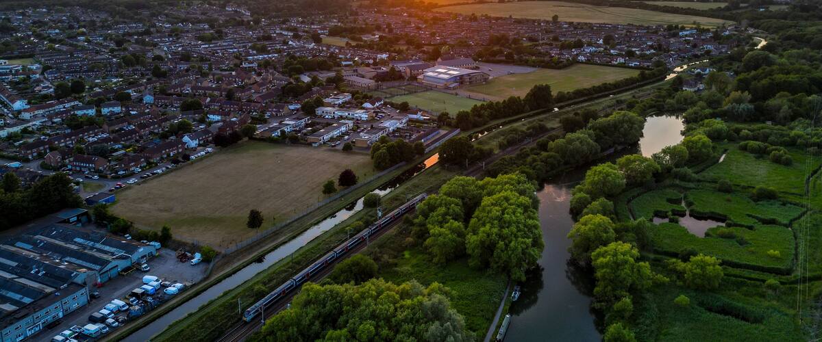A sunset over a town with a river, train tracks, and surrounding greenery.