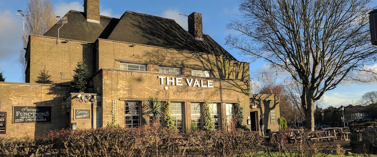 A brick building labeled "The Vale" with ivy and a stone wall in the foreground.