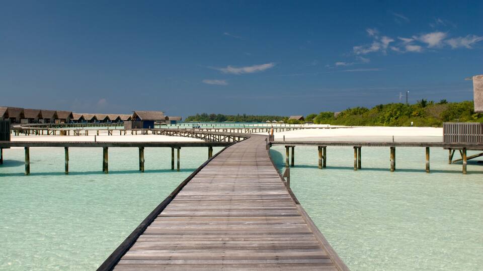 A wooden pier leading to overwater bungalows in clear turquoise waters.