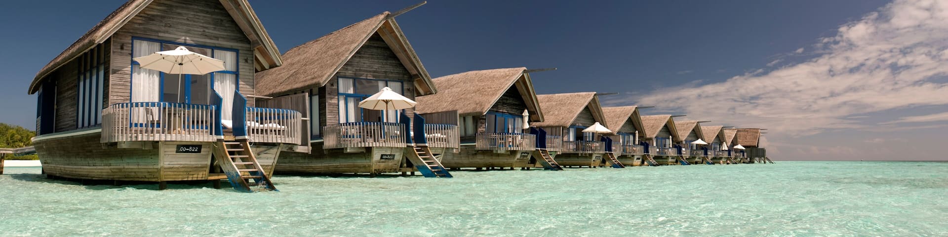 Overwater bungalows with thatched roofs and wooden railings on a clear turquoise sea.
